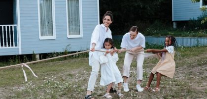 A happy family enjoys a game of tug of war in a grassy field by a house.