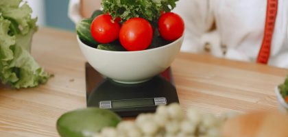 Colorful fresh vegetables including tomatoes and cucumbers on a kitchen scale for healthy eating.